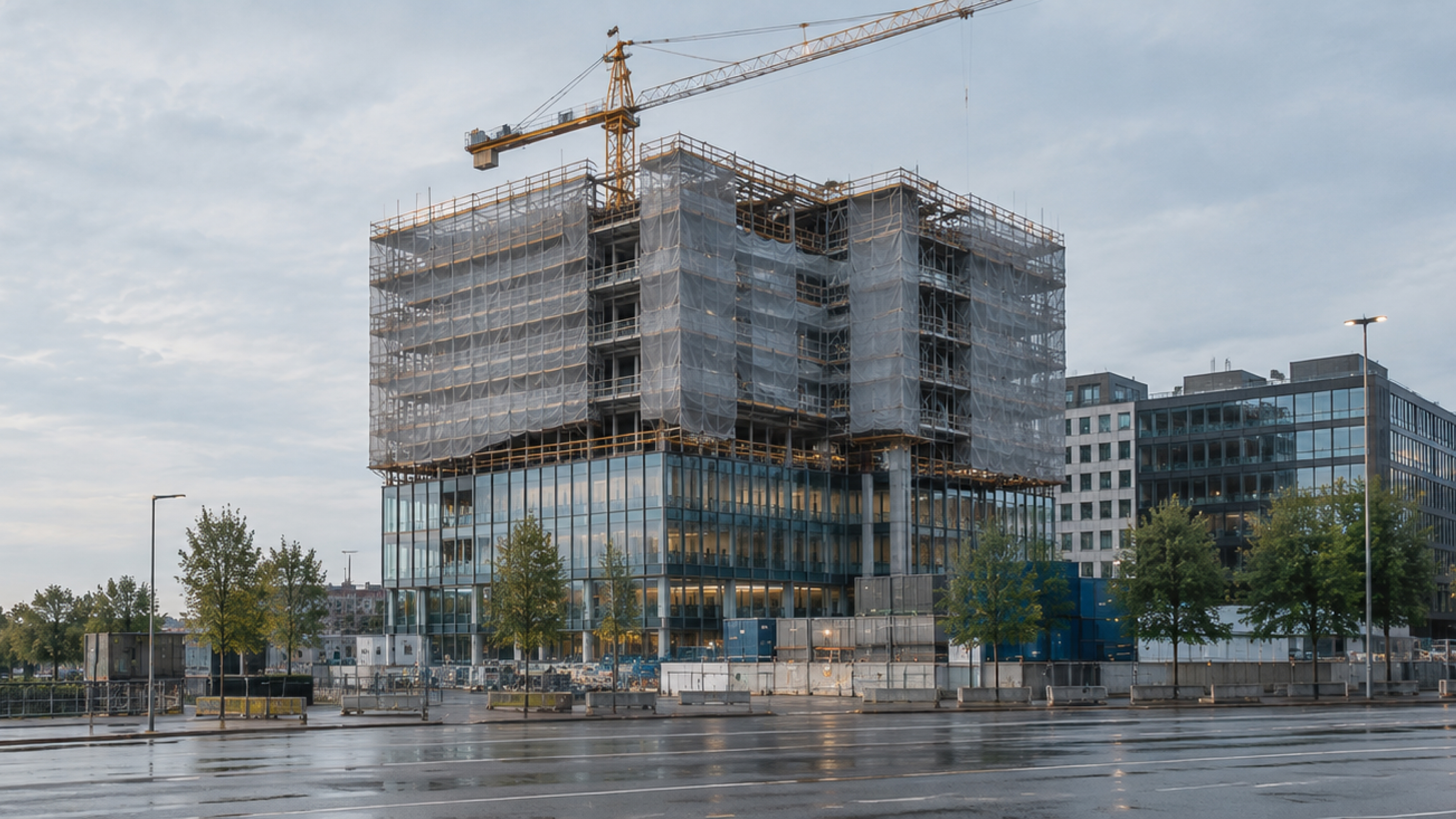 A high-rise under construction, its upper floors wrapped in scaffolding and climbing screens, with a crane standing on the roof.